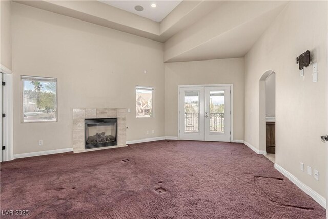 unfurnished living room with baseboards, carpet floors, a towering ceiling, and a healthy amount of sunlight