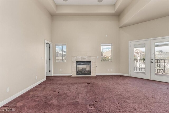 unfurnished living room featuring carpet floors, french doors, a fireplace, a high ceiling, and baseboards