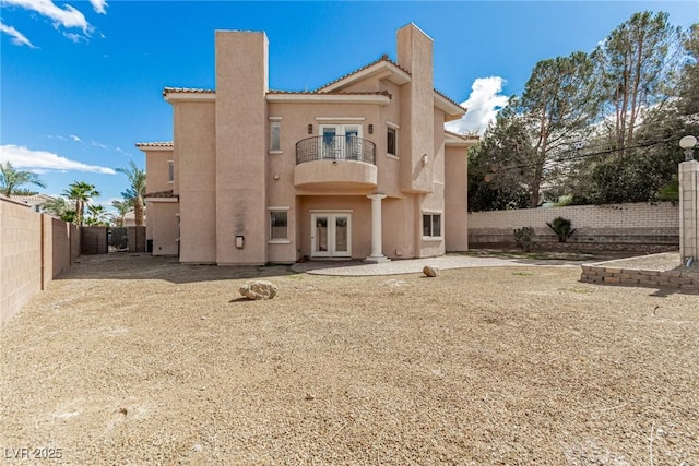 rear view of property with french doors, a tile roof, stucco siding, a balcony, and a fenced backyard