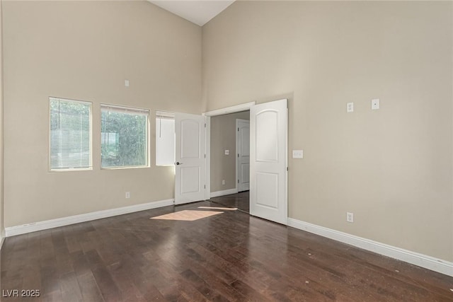 spare room with a high ceiling, baseboards, and wood finished floors