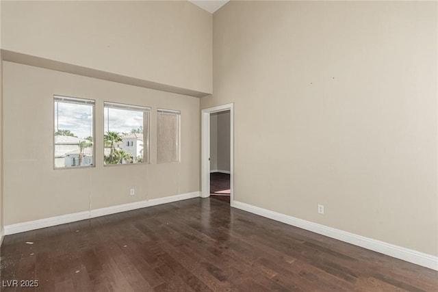 unfurnished room with a high ceiling, dark wood finished floors, and baseboards