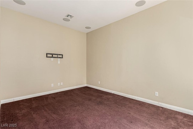 spare room featuring dark colored carpet, visible vents, and baseboards