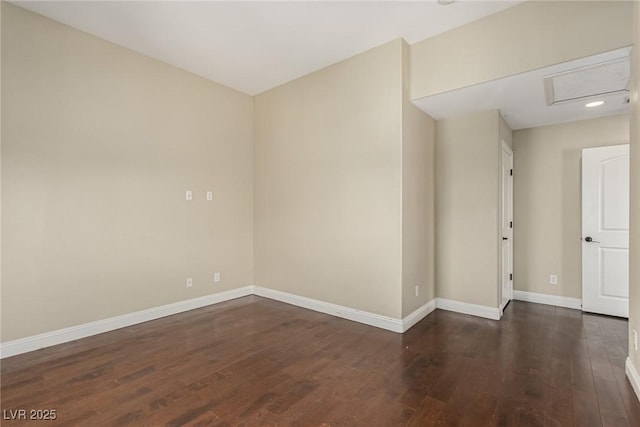 empty room featuring dark wood-style floors, attic access, and baseboards