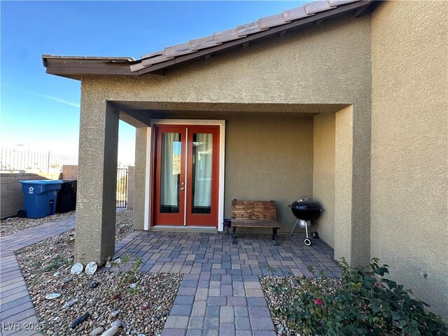 property entrance featuring french doors, a patio area, fence, and stucco siding