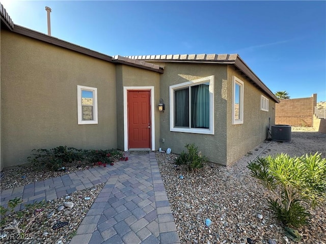 property entrance featuring fence, cooling unit, and stucco siding