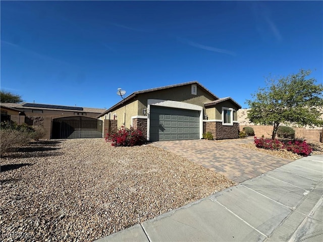 view of front of property with decorative driveway, stucco siding, a gate, a garage, and stone siding