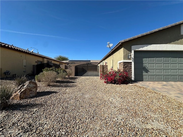 view of side of property with stone siding, decorative driveway, a gate, and stucco siding