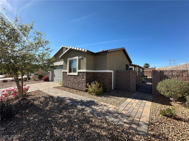 view of side of property with a garage, stone siding, a gate, fence, and stucco siding