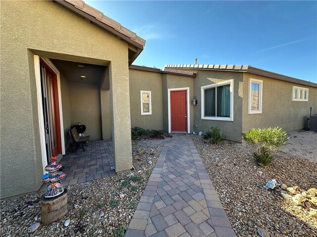 view of exterior entry featuring central air condition unit, a patio, and stucco siding