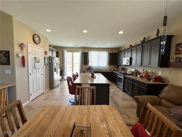 kitchen with light tile patterned flooring, recessed lighting, stainless steel appliances, a kitchen island, and light stone countertops