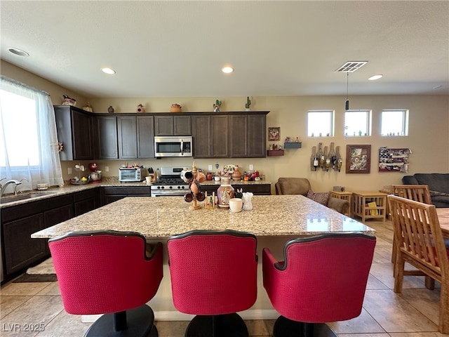 kitchen featuring visible vents, a kitchen island, light stone countertops, stainless steel appliances, and a sink