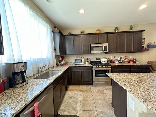 kitchen featuring light stone counters, light tile patterned floors, stainless steel appliances, a sink, and dark brown cabinetry