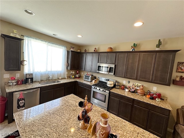 kitchen with appliances with stainless steel finishes, a sink, light stone counters, and dark brown cabinetry