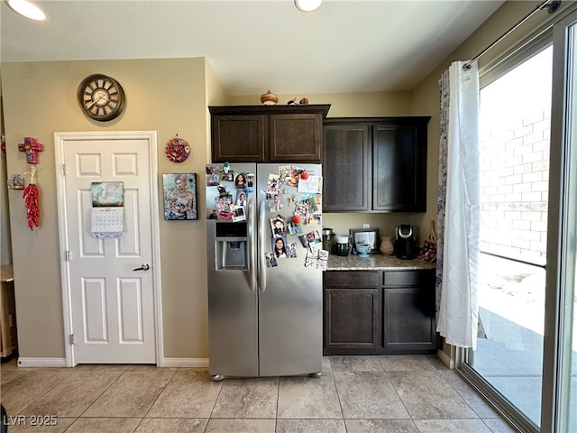 kitchen featuring light tile patterned flooring, baseboards, dark brown cabinets, stainless steel refrigerator with ice dispenser, and light stone countertops