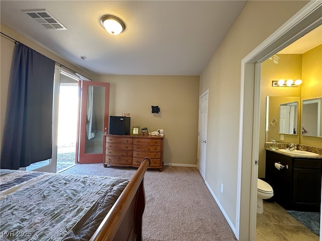 bedroom with light colored carpet, visible vents, connected bathroom, a sink, and baseboards