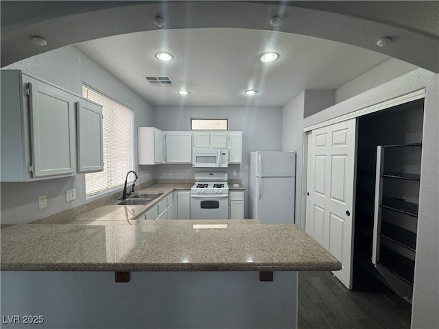 kitchen featuring white appliances, a breakfast bar area, visible vents, a peninsula, and a sink