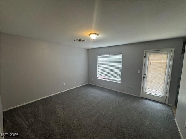 spare room with visible vents, baseboards, and dark colored carpet