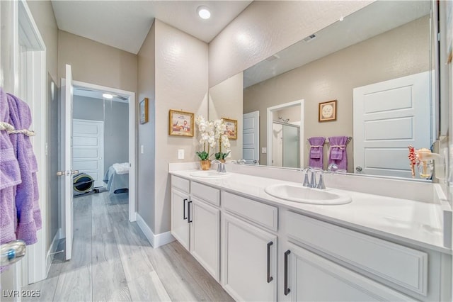 bathroom with a stall shower, wood finished floors, a sink, and double vanity