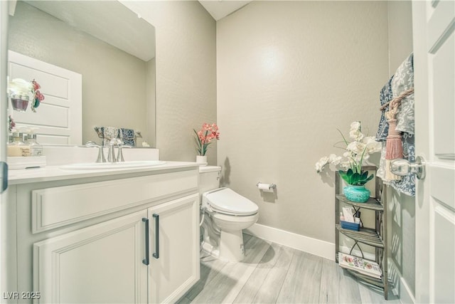 bathroom featuring baseboards, vanity, toilet, and wood finished floors