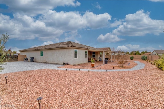 rear view of property with stucco siding, a tiled roof, fence, and a patio