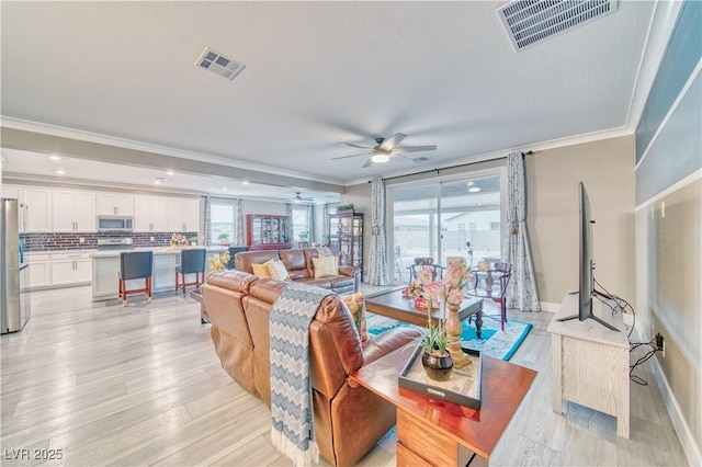 living area with ornamental molding, light wood-type flooring, and visible vents