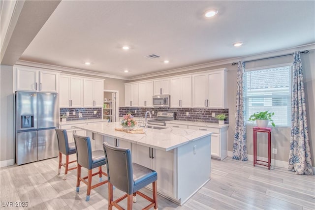 kitchen featuring visible vents, an island with sink, stainless steel appliances, a kitchen bar, and white cabinetry