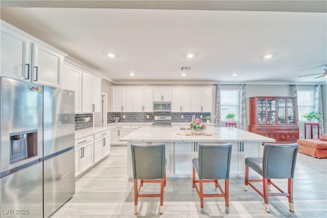 kitchen with stainless steel appliances, white cabinetry, visible vents, and decorative backsplash