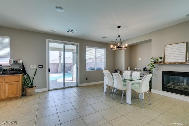 dining space featuring light tile patterned flooring, visible vents, baseboards, a glass covered fireplace, and an inviting chandelier