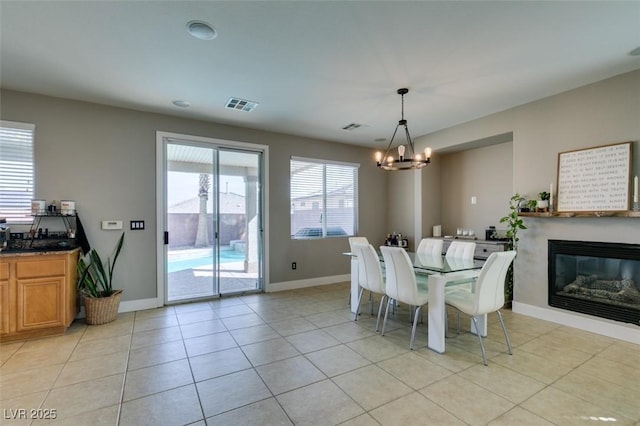 dining space with a chandelier, light tile patterned floors, baseboards, and a glass covered fireplace