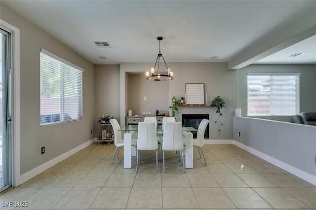 dining space featuring light tile patterned flooring, baseboards, a chandelier, and a glass covered fireplace