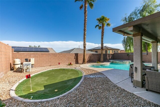 fenced backyard with an area to practice putting, a patio, and a pool with connected hot tub