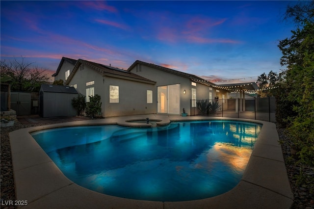 pool at dusk featuring an outbuilding, a patio, a storage unit, a pool with connected hot tub, and fence