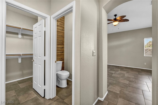 bathroom with a ceiling fan, a walk in closet, baseboards, and toilet