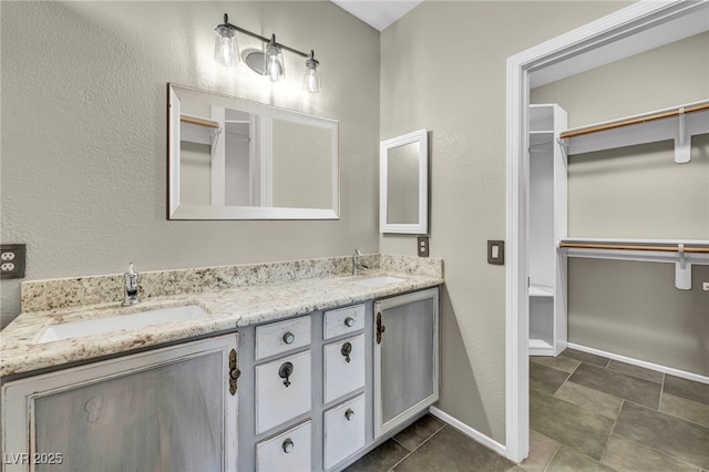 bathroom with double vanity, a spacious closet, baseboards, and a sink