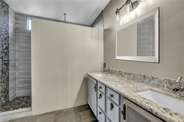 bathroom with a textured wall, double vanity, walk in shower, and a sink