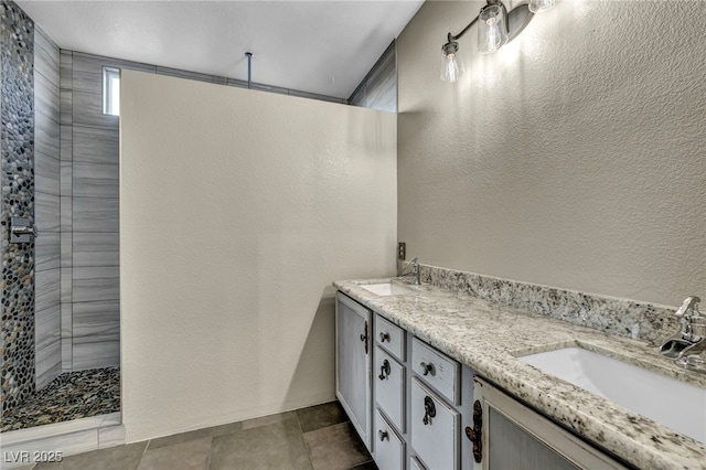 full bath with double vanity, walk in shower, a sink, and a textured wall