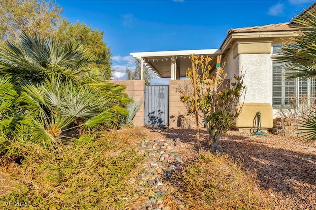 property entrance featuring a gate, fence, and stucco siding