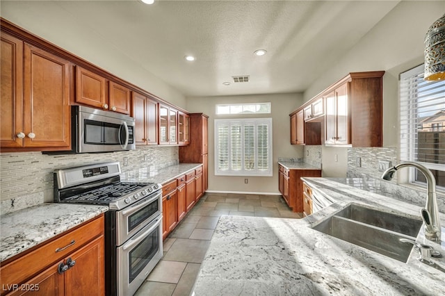 kitchen featuring light stone counters, stainless steel appliances, visible vents, a sink, and baseboards