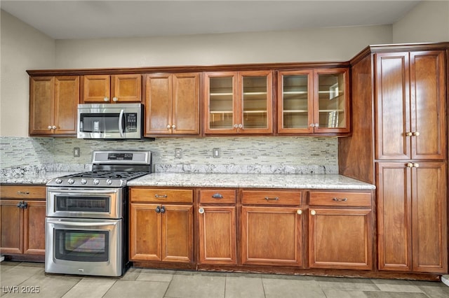 kitchen with stainless steel appliances, light stone countertops, glass insert cabinets, and decorative backsplash