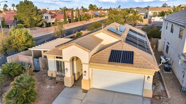 view of front of property with a garage, driveway, a residential view, roof mounted solar panels, and stucco siding