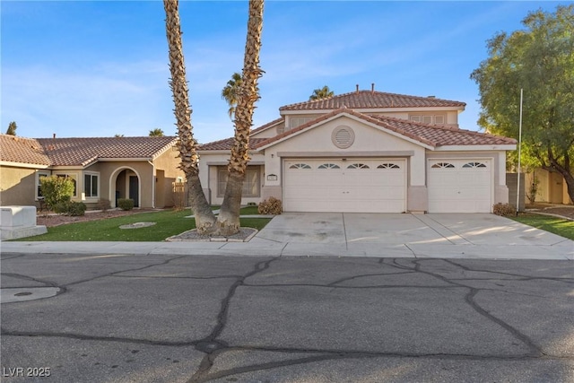 mediterranean / spanish house with driveway, an attached garage, a tile roof, and stucco siding