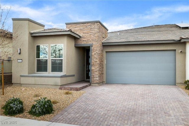 view of front of house with decorative driveway, stone siding, an attached garage, and stucco siding