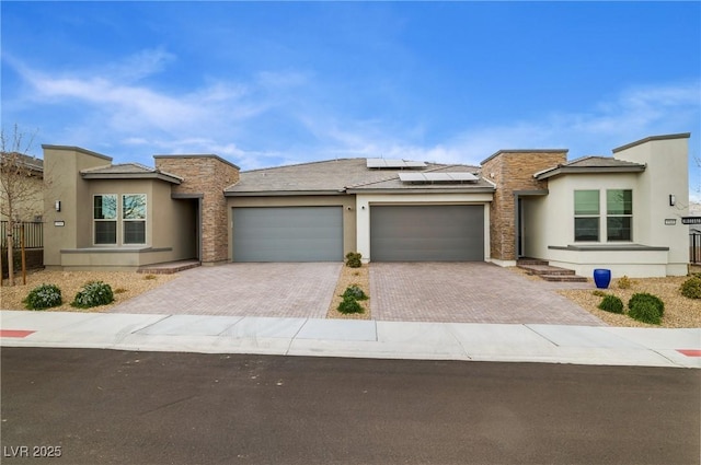 prairie-style house with an attached garage, solar panels, stone siding, decorative driveway, and stucco siding