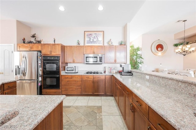 kitchen with hanging light fixtures, an inviting chandelier, light stone counters, and stainless steel appliances