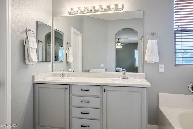 full bathroom featuring a sink, a relaxing tiled tub, ceiling fan, and double vanity