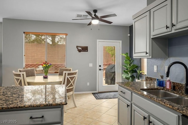 kitchen featuring visible vents, gray cabinets, a sink, dark stone countertops, and light tile patterned flooring