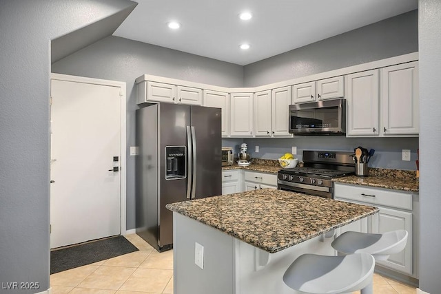 kitchen featuring light tile patterned floors, a kitchen island, dark stone counters, appliances with stainless steel finishes, and a kitchen breakfast bar