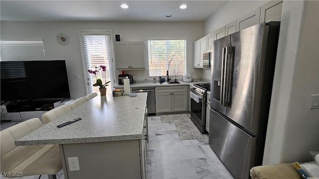 kitchen featuring appliances with stainless steel finishes, a breakfast bar, marble finish floor, a sink, and recessed lighting