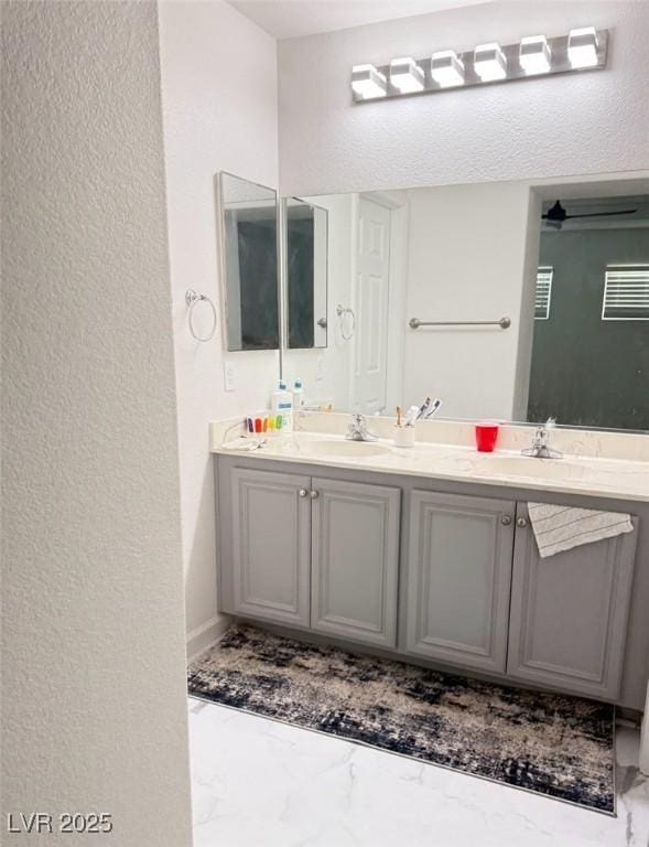 full bath featuring a textured wall, marble finish floor, double vanity, and a sink