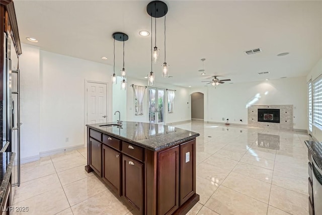 kitchen featuring arched walkways, a tile fireplace, a sink, visible vents, and dark stone counters